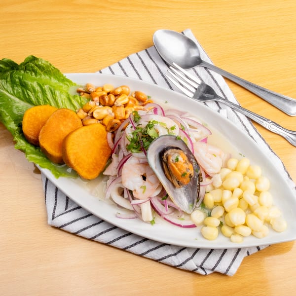 A white platter of ceviche with shrimp, squid, mussels, red onion, sweet potato, and corn.