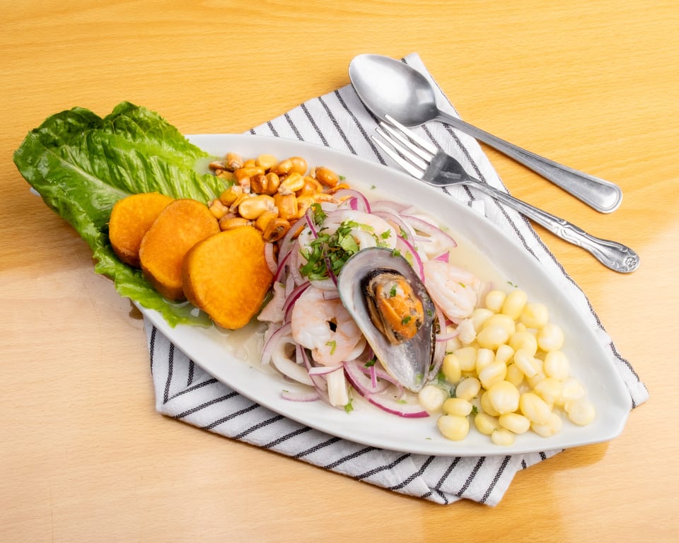 A white platter of ceviche with shrimp, squid, mussels, red onion, sweet potato, and corn.