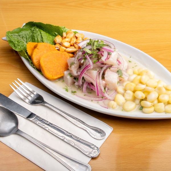 Peruvian ceviche with fish, red onion, corn, sweet potato, and lettuce on a white plate.