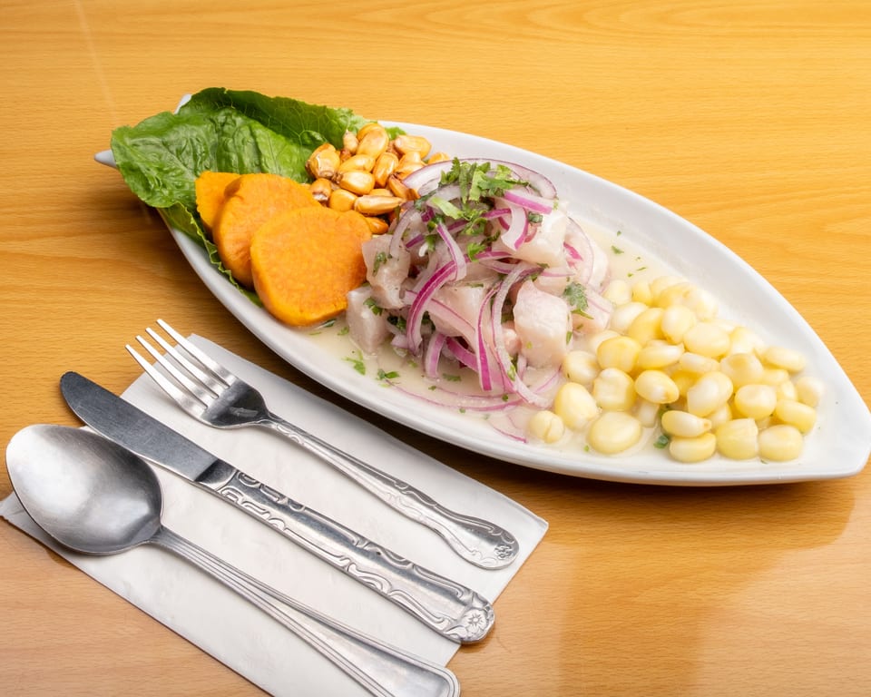 Peruvian ceviche with fish, red onion, corn, sweet potato, and lettuce on a white plate.