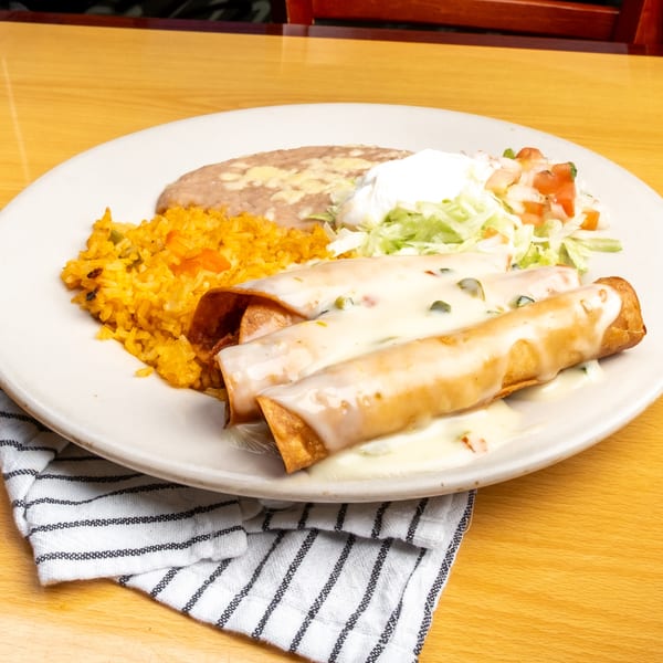 Three taquitos covered in white sauce, served with rice, refried beans, and a side salad.