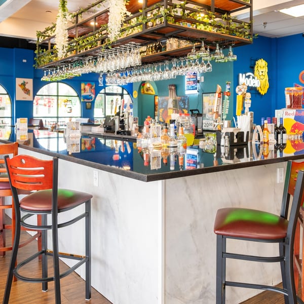 A vibrant bar with blue walls, a dark countertop, bar stools, and hanging glasses.