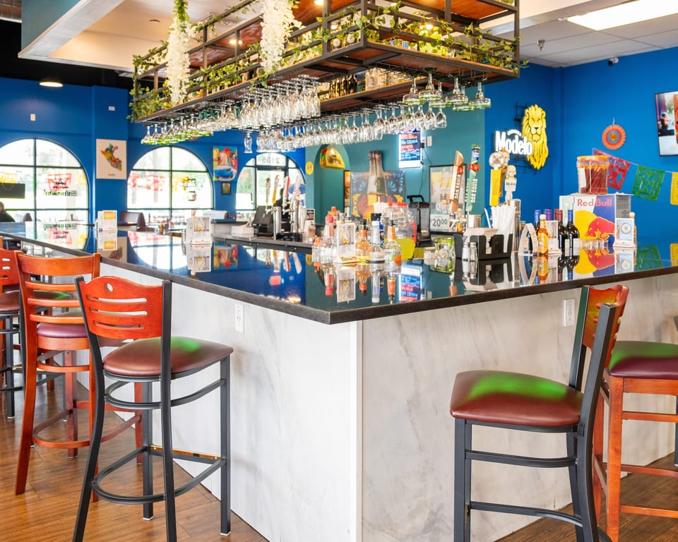 A vibrant bar with blue walls, a dark countertop, bar stools, and hanging glasses.