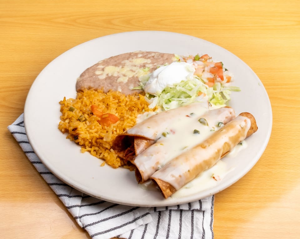 Three taquitos covered in white sauce, with rice, refried beans, and pico de gallo.