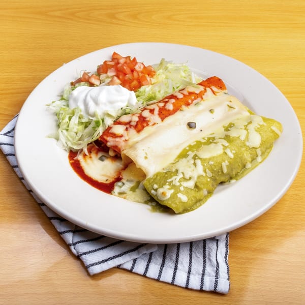 Two enchiladas, one red and one green, with shredded lettuce, diced tomatoes, and sour cream.