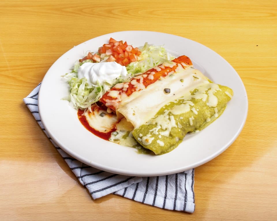 Two enchiladas, one red and one green, with shredded lettuce, diced tomatoes, and sour cream.