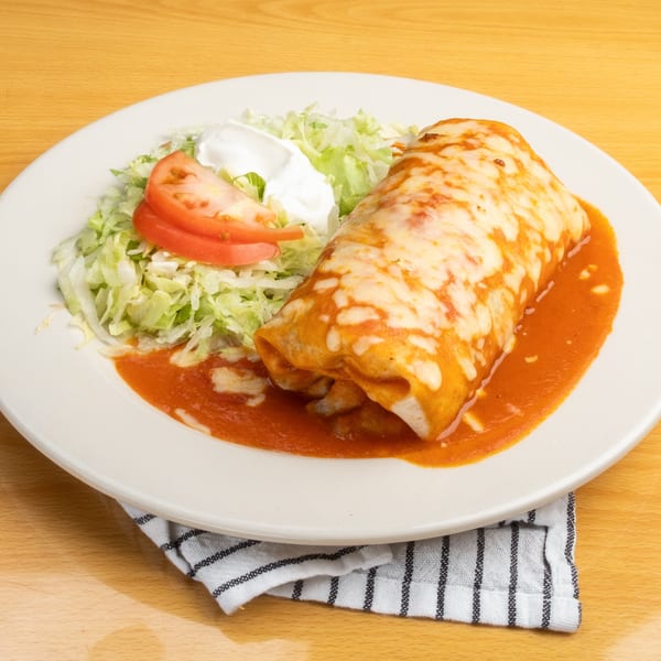 A large burrito covered in melted cheese and red sauce, with shredded lettuce, sour cream, and tomato.