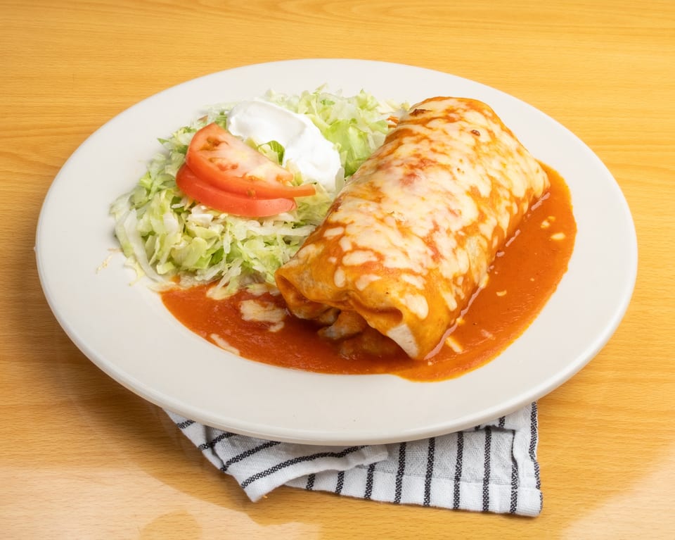 A large burrito covered in melted cheese and red sauce, with shredded lettuce, sour cream, and tomato.