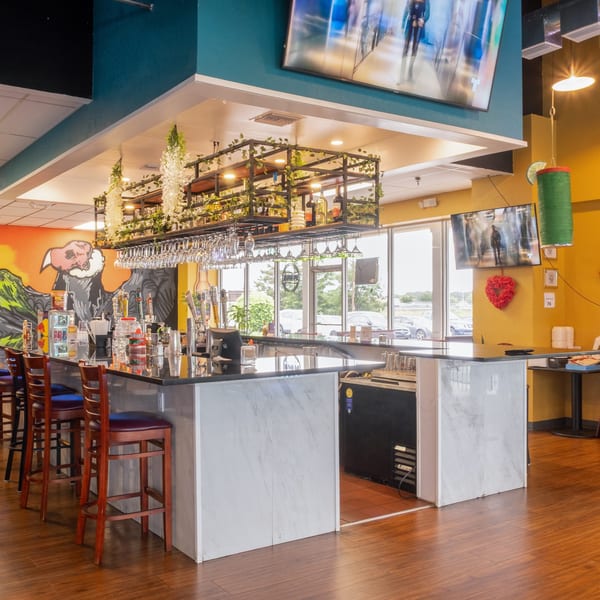 A vibrant restaurant interior features a long bar with stools, a colorful mural, and decorative lighting.