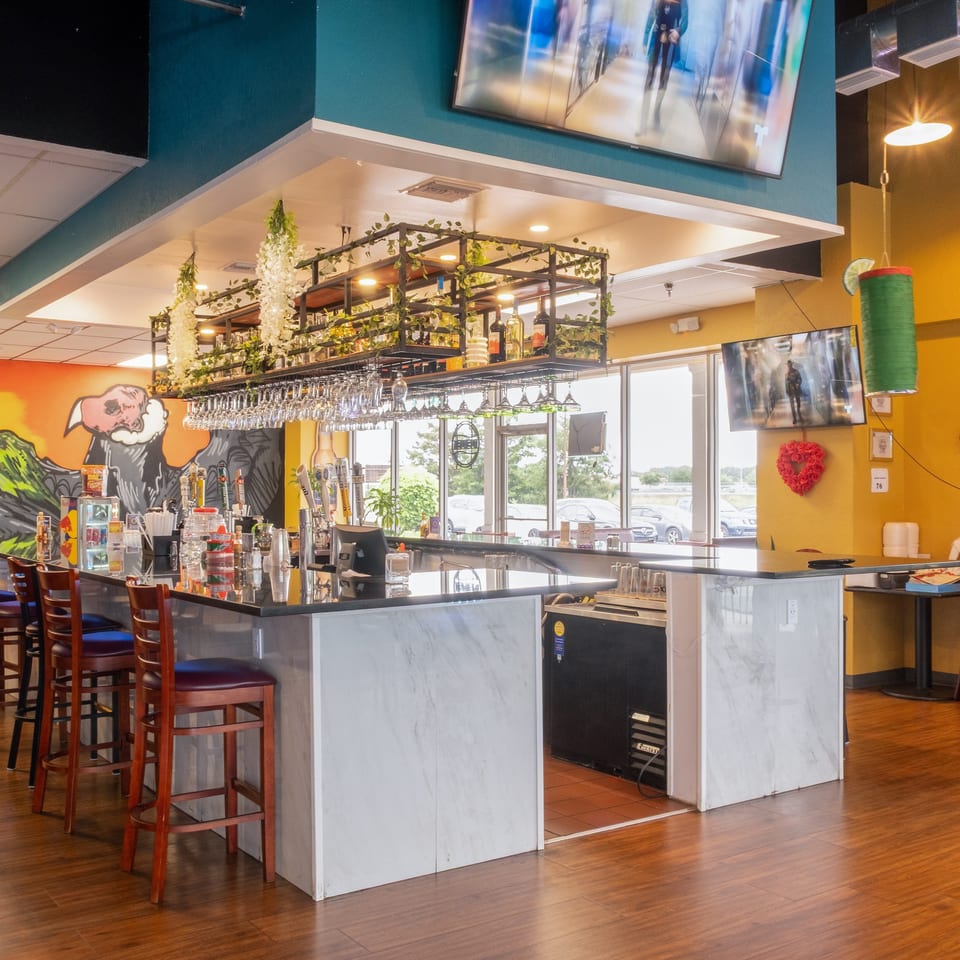 A vibrant restaurant interior features a long bar with stools, a colorful mural, and decorative lighting.