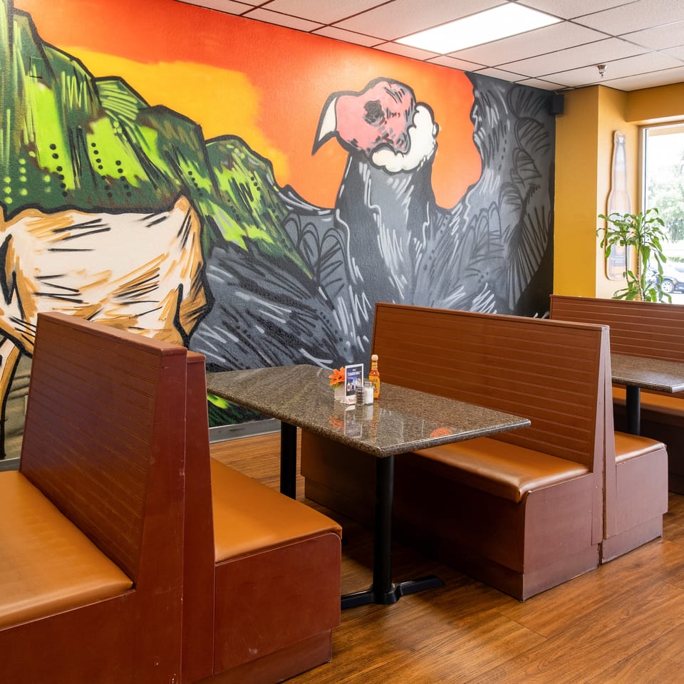 Restaurant interior with brown booths, granite tables, and a vibrant mural of a llama and condor.