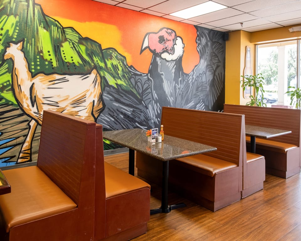 Restaurant interior with brown booths, granite tables, and a vibrant mural of a llama and condor.