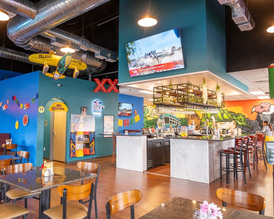 A vibrant Mexican restaurant interior with colorful murals, a bar, tables, and decorative elements.