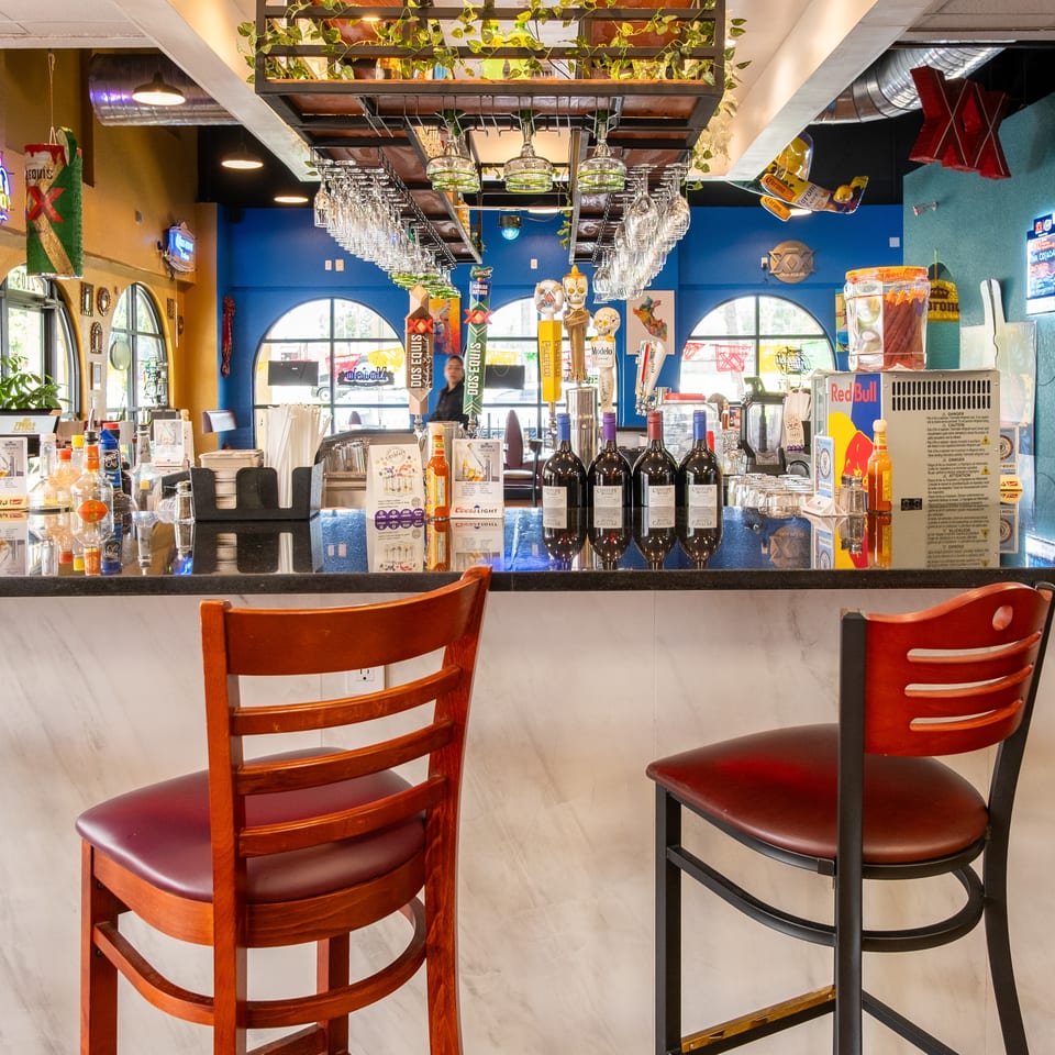 A vibrant restaurant bar with bottles, beer taps, wine glasses, and bar stools.