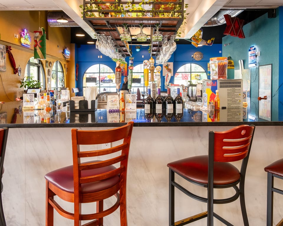 A vibrant restaurant bar with bottles, beer taps, wine glasses, and bar stools.