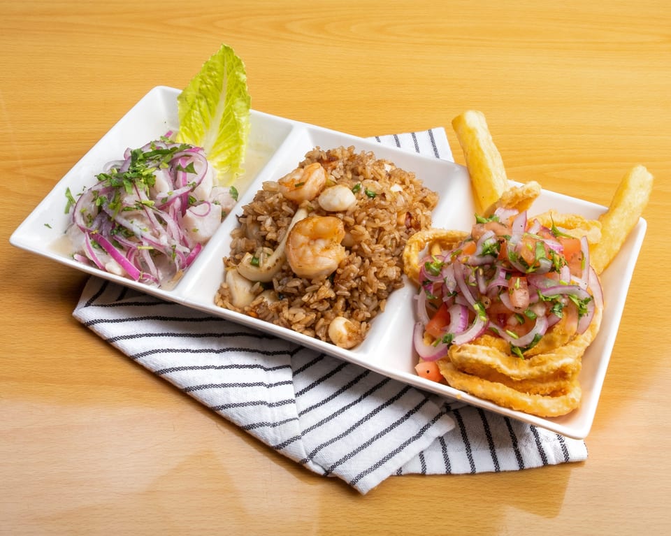 A white rectangular plate with three sections of Peruvian dishes on a wooden table.