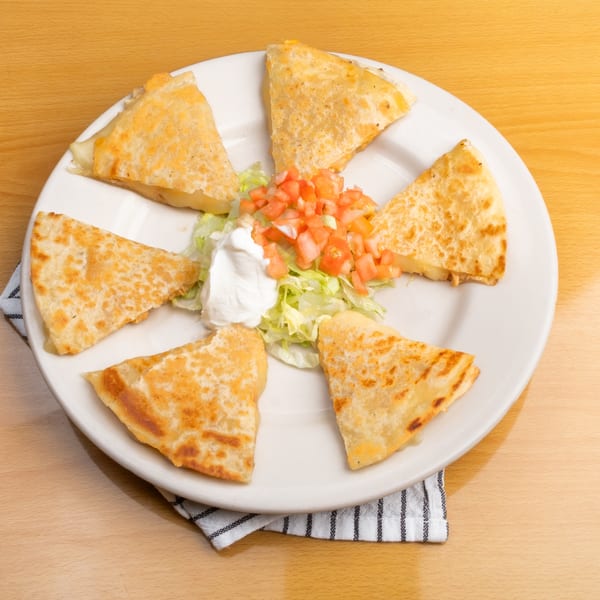 Six quesadilla wedges arranged on a white plate with a side of lettuce, diced tomatoes, and sour cream.